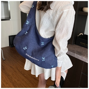 Sac cabas en toile bleu foncé avec broderie cerise et lettrage blanc porté à l'épaule