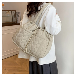 Macro view of the quilted leaf pattern and drawstring closure on this beige tote bag