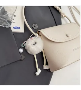 Close-up of beige lychee texture bag with plush doll charm and embossed logo detail