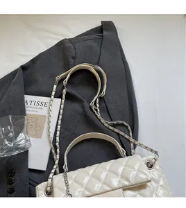 Detailed top view of white quilted crossbody bag with silver chain on grey blazer