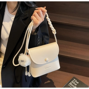 Detail of off-white leather bucket bag with braided handle and plush toy charm on stairs