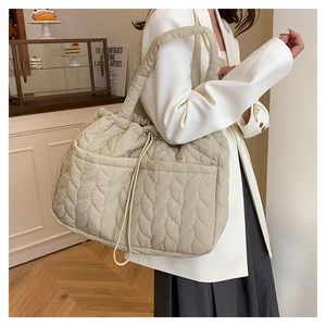 Detail of beige quilted tote bag showing leaf pattern stitching and side drawstring