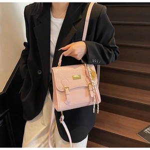 Petit sac bandoulière rose clair porté avec un blazer noir et un pantalon blanc élégant