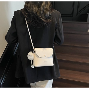 Detailed back view of white litchi pattern bucket bag with fluffy charm on a staircase
