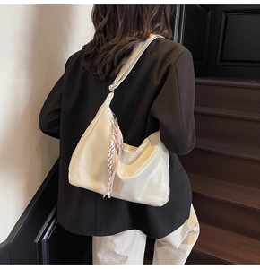 Minimalist beige dumpling bag with woven knot detail shown in a stylish commute setting
