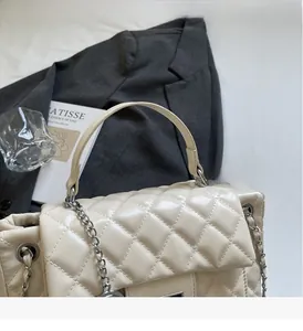 Detail of quilted beige shoulder bag with metal chain strap and leather top handle