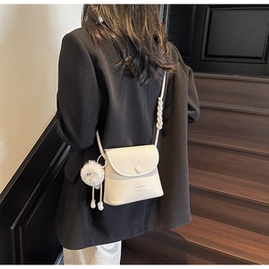 Detail of off-white lychee grain leather crossbody bag with woven rope strap and plush pompom