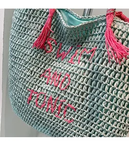 Detailed view of mint green straw tote bag with pink SWIM AND TONIC embroidery and tassels