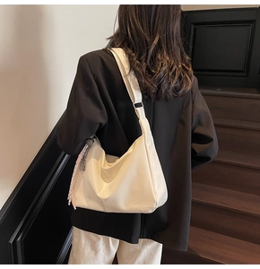Detail of off-white hobo shoulder bag with woven tassel charm on a female model
