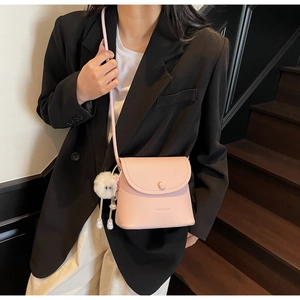Pink lychee grain leather bucket bag featuring a white plush pendant and adjustable strap