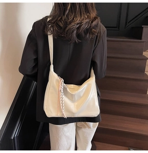 Detail of cream crossbody dumpling bag with woven pendant on black blazer and white pants