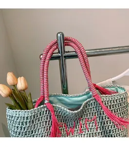 Close-up of mint green straw bag with pink tassel and blue woven handle details