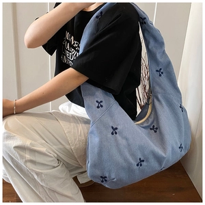 Gros plan du sac fourre-tout en jean bleu clair avec broderies cerises et zip à anneau