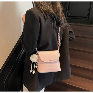 Detail of pink faux leather crossbody bucket bag with braided strap and plush doll charm