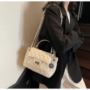 Close-up of beige quilted leather handbag with silver twist lock and chain strap on model