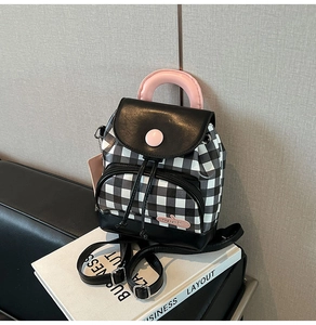 Detail of a mini gingham backpack with pink handle and leather trim on a book prop