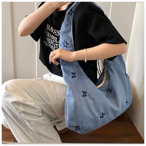Détail du sac hobo en toile bleue avec broderie cerise porté par un mannequin