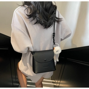 Detail of black pebbled leather crossbody bag with a fluffy white charm and woven strap
