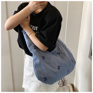 Détail du sac hobo en jean bleu avec broderies cerises et bandoulière large confortable