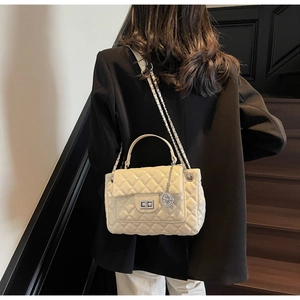 Detail of beige quilted chain bag featuring silver turn-lock and round charm on model
