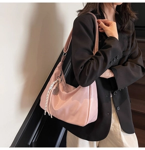 Detail of pink hobo bag featuring woven tassels and silver metal tag charm