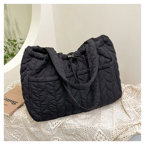 Detail of black quilted tote bag with wave stitching and side pocket on a table