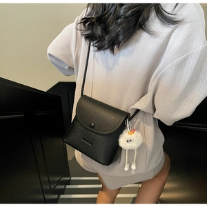 Detail of black pebbled leather mini crossbody bag with a white plush doll charm