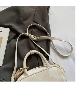 Detail der weißen geprägten Handtasche mit gewebtem Anhänger auf grauem Sakko