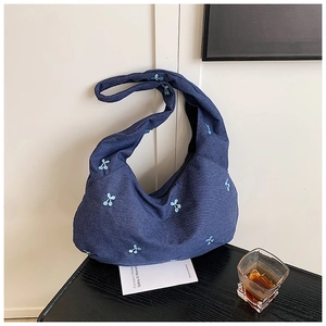 Détail du sac bandoulière en denim bleu marine avec broderie cerise sur bois texturé