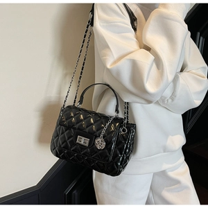 Close-up of black quilted leather handbag with silver chain strap and metal charm on a model