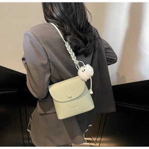 Detail of mint green leather bucket bag with woven strap and white plush charm on a model