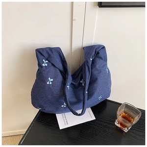Gros plan d'un sac cabas en toile bleu marine avec motifs cerises brodés sur une table