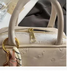 Detail des glatten goldenen Reißverschlusses und Prägetextur auf der cremefarbenen Tasche