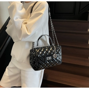Detail of black quilted chain bag with silver clasp shown on a crossbody model