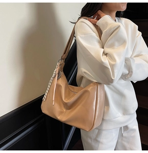 Detail of beige large capacity shoulder bag featuring woven rope and leather tassel charms