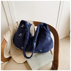 Broderie détaillée de cerises bleu clair et texte blanc sur un sac hobo en toile bleu marine