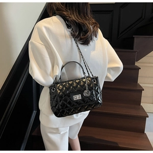 Detail view of a black quilted shoulder bag with silver chain strap on a modern staircase