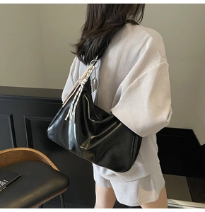 Large black crossbody dumpling bag with metallic hardware shown on a model