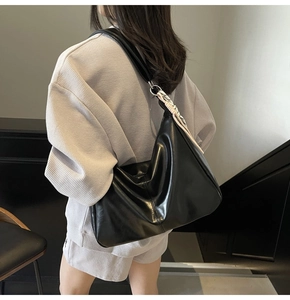 Side view of a large black PU leather tote bag worn by a model in a minimalist setting