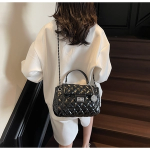 Detail of black quilted chain bag featuring silver twist lock and polished finish