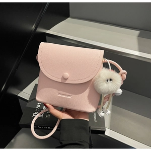Close-up of pink litchi grain leather crossbody bag with fluffy white pompom charm