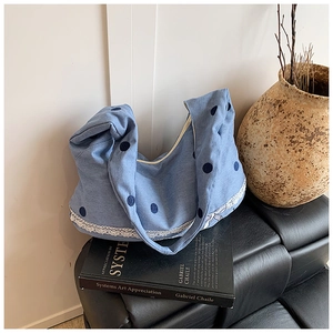 Vue macro du sac à bandoulière en denim à pois bleus avec dentelle blanche sur canapé