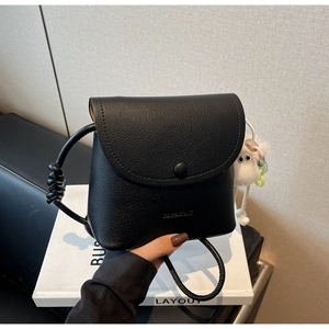 Detail of black lychee grain leather bucket bag with plush toy charm and knotted strap