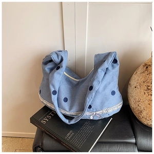 Détail du sac en toile bleu clair à pois foncés avec bordure en dentelle et nœud décoratif