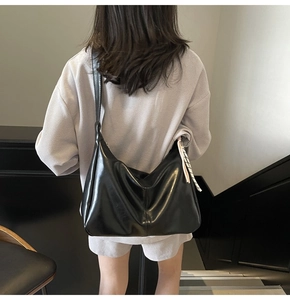 Minimalist black half-moon shoulder bag with decorative striped scarf on strap
