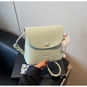 Detail of mint green bucket bag featuring lychee grain leather and a white plush ball charm