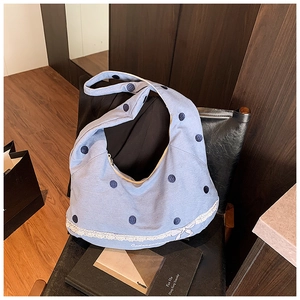 Détail d'un sac hobo en toile bleu clair à pois avec dentelle et nœud sur chaise