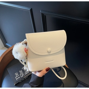 Detail of white lychee leather bucket bag with fuzzy pompom and magnetic flap closure
