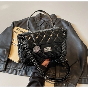 Close-up of black quilted glossy handbag with silver twist lock and chain strap detail
