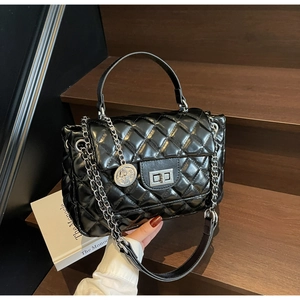 Detail of black quilted leather handbag with silver hardware and coin pendant on wood